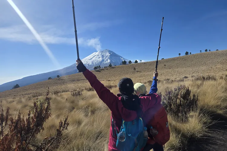 xcursionista levantando los brazos frente al volcán Iztaccíhuatl