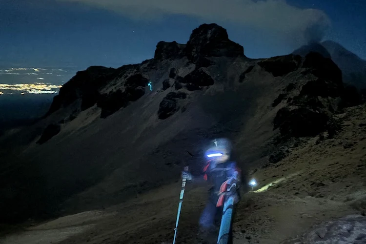 Mountaineer climbing Iztaccíhuatl at night with headlamp illuminating the trail