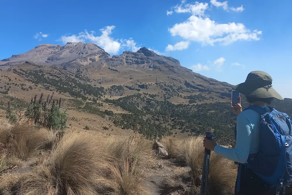 Traveler hiking in Iztaccíhuatl Volcano with trekking poles and panoramic views of the mountain – Mexico City day tour